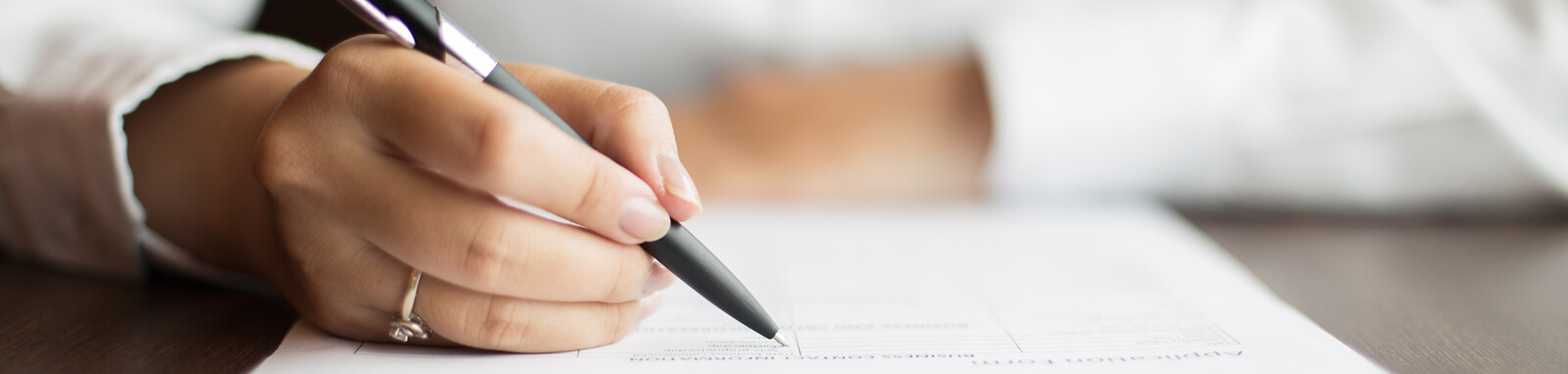 Imagem de uma mão com uma caneta assinando um contrato.